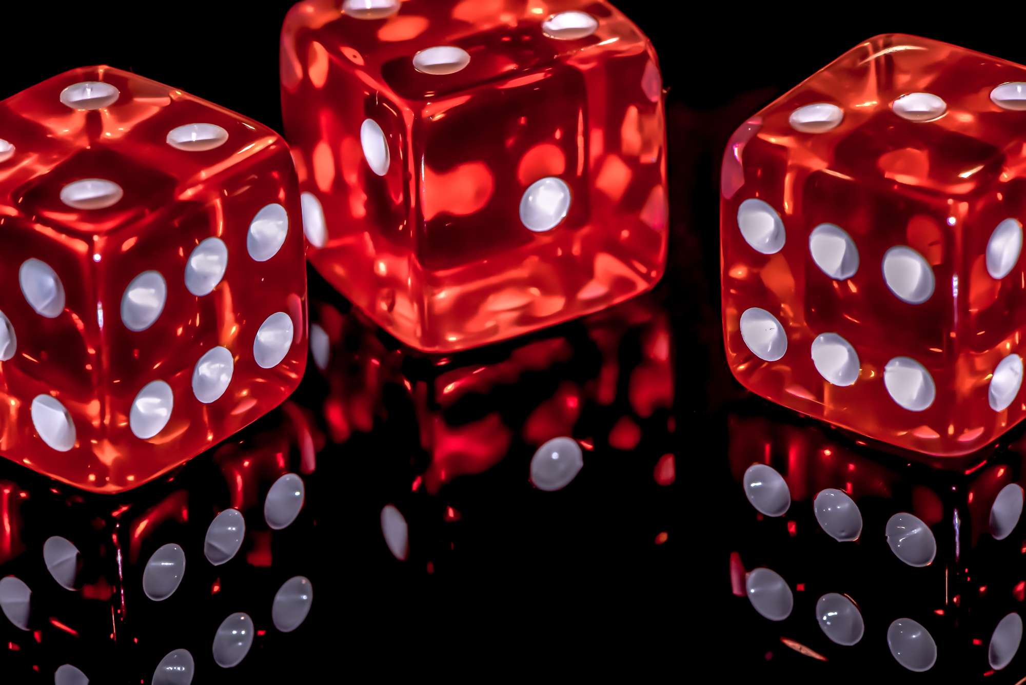 Close-up of three red dice on a dark, reflective surface.