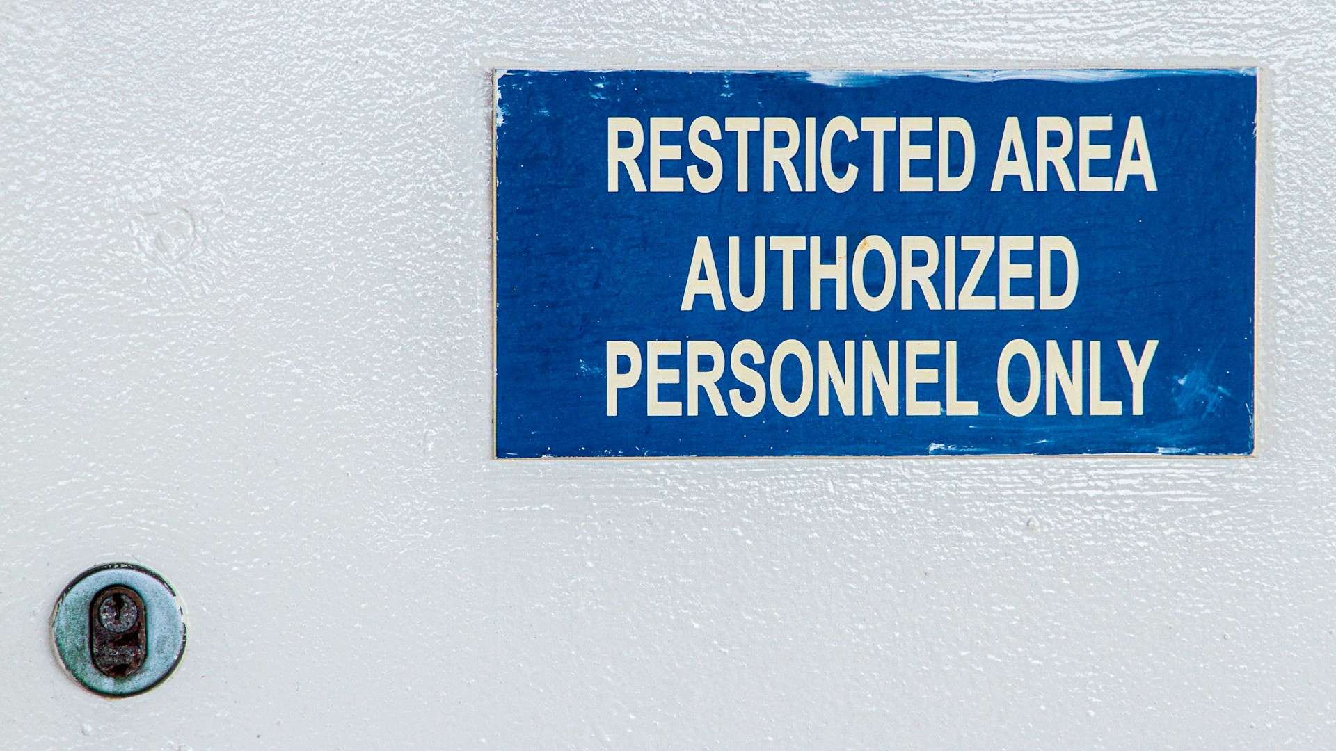 A blue sign on a white wall stating restricted area authorized personnel only