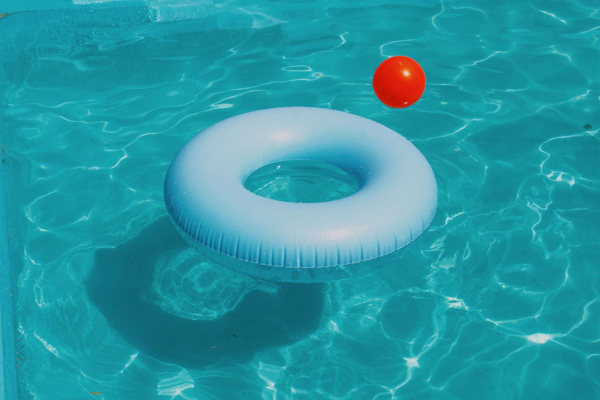 A blue swimming ring and a red plastic ball swimming in a pool
