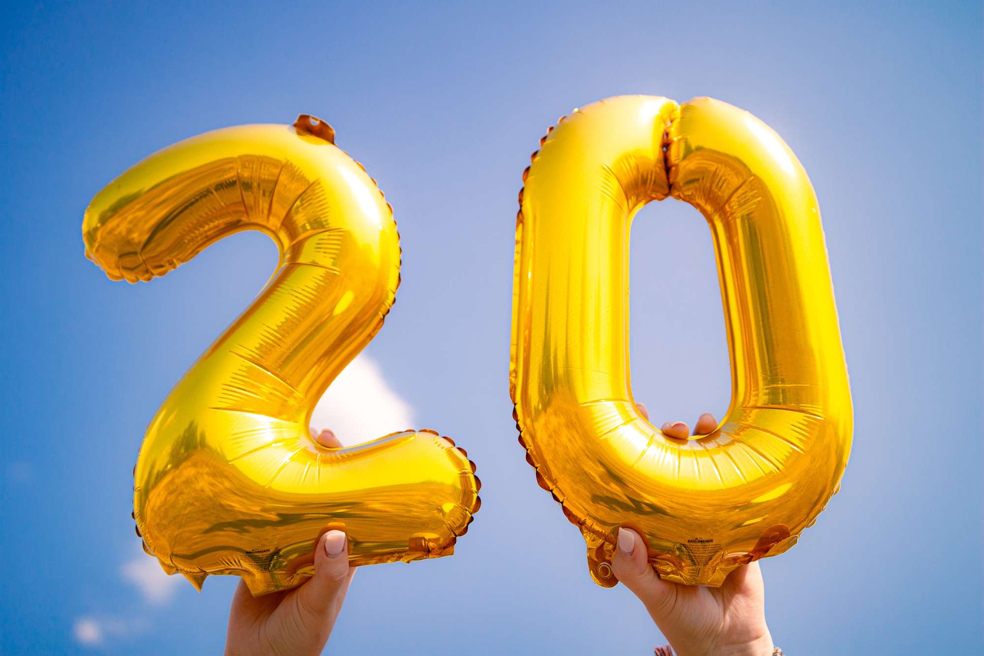 Two hands, each holding a large ballon in the shape of a digit, forming the number 20